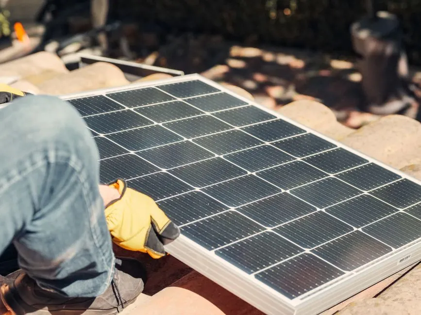 A worker installs a solar panel on a sunlit rooftop, exemplifying renewable energy.